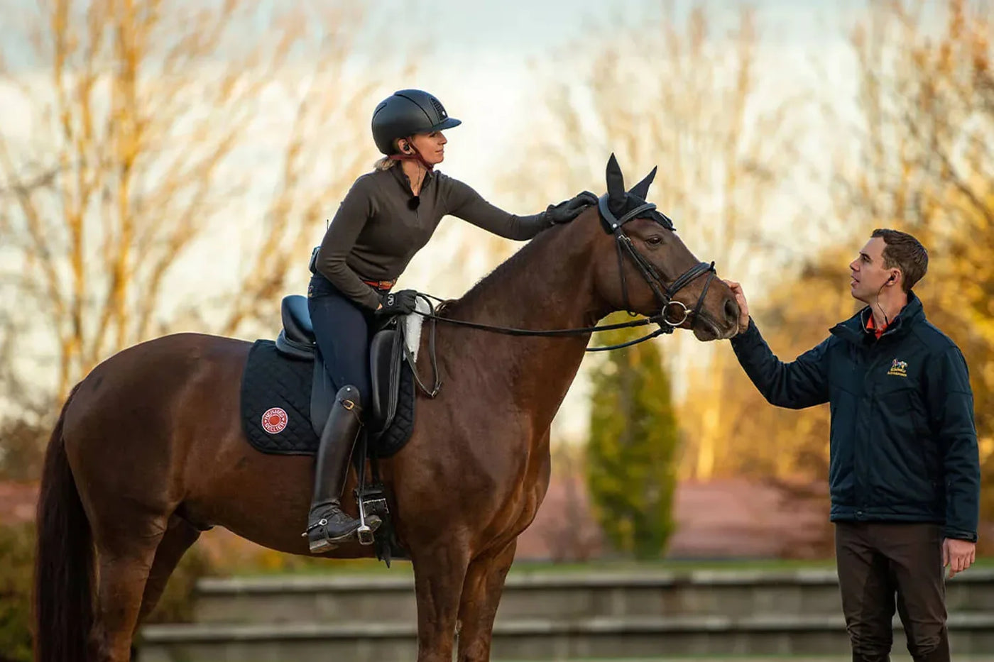 Reiterin auf braunem Pferd wird von Trainer geprüft, Perfektion im Reitsport - Das Fitness-Programm für Reiter.