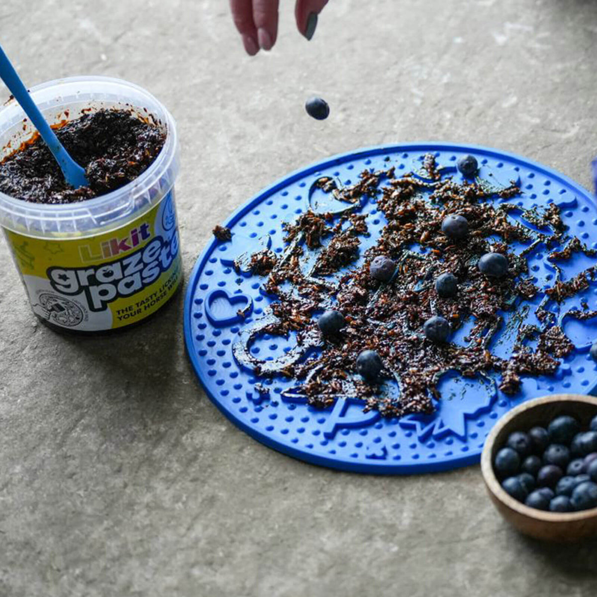 Beschäftigungsmatte Likit Graze Maze Schleckmatte, Blau, mit Futter belegt und Becher daneben.