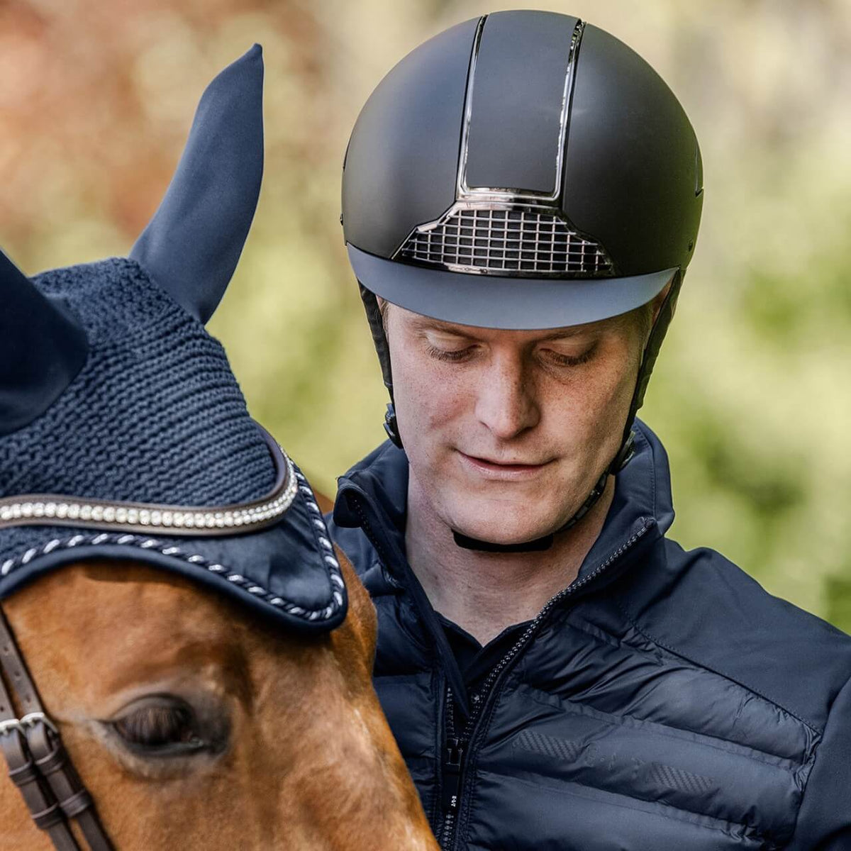 Reithelm Unisex H24 Chrome, Schwarz, Person trägt den Helm neben einem Pferd.