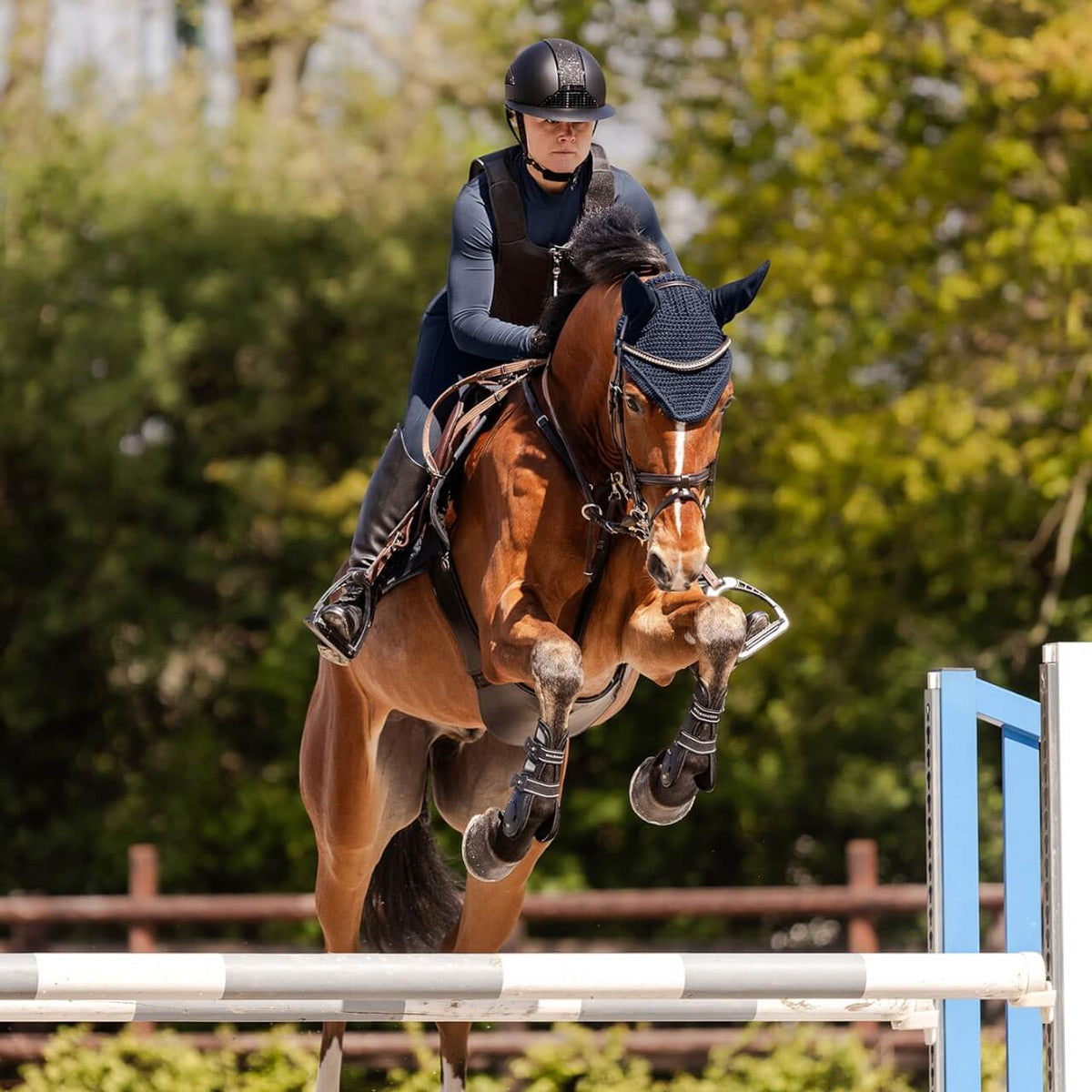 Reithelm Damen H24 Lady Shine, Schwarz, Reiterin springt mit Pferd im Parcours.