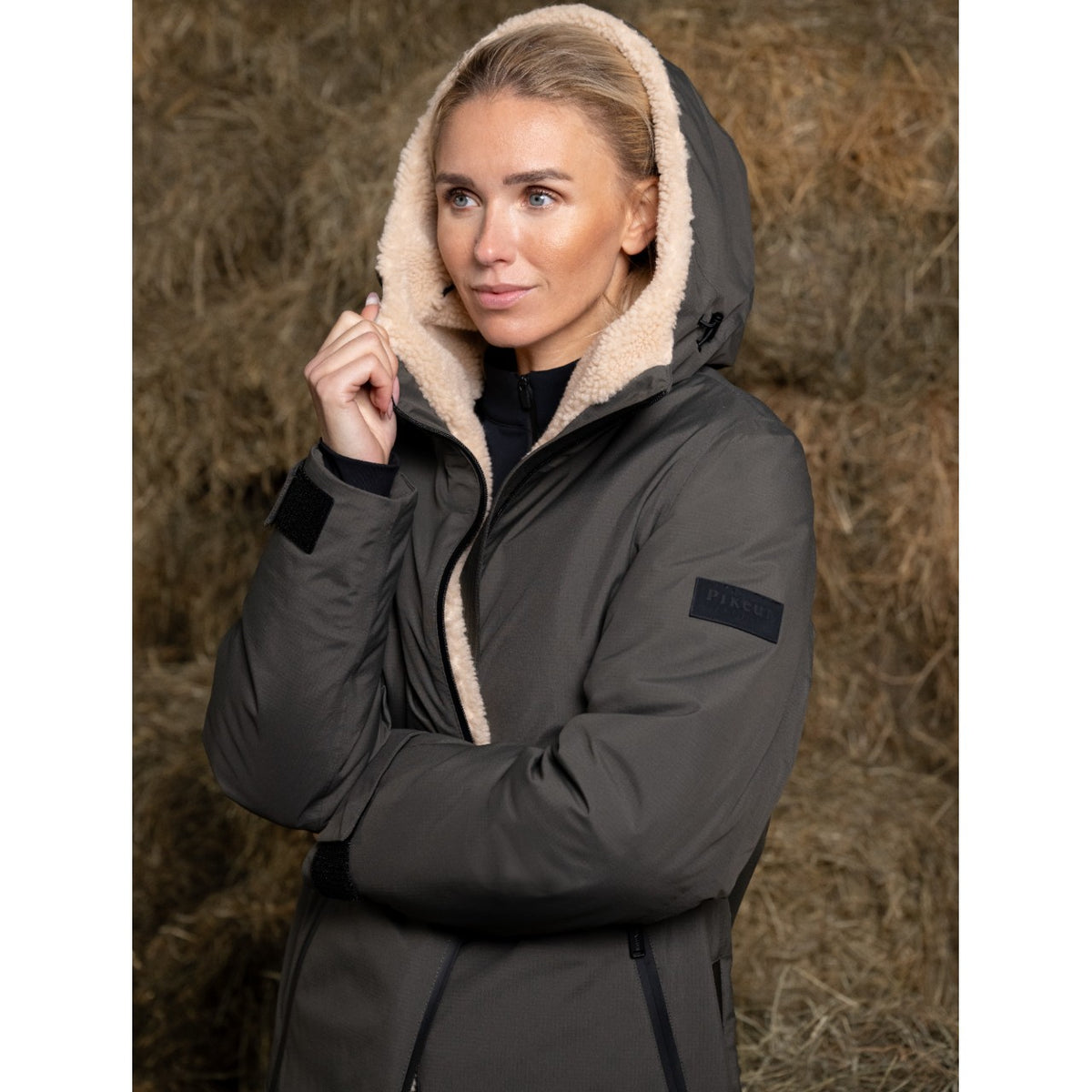Pikeur Regenmantel Damen Sports HW 2025 Mantel, Dunkelgrau, Frau trägt den Mantel vor Heuballen.