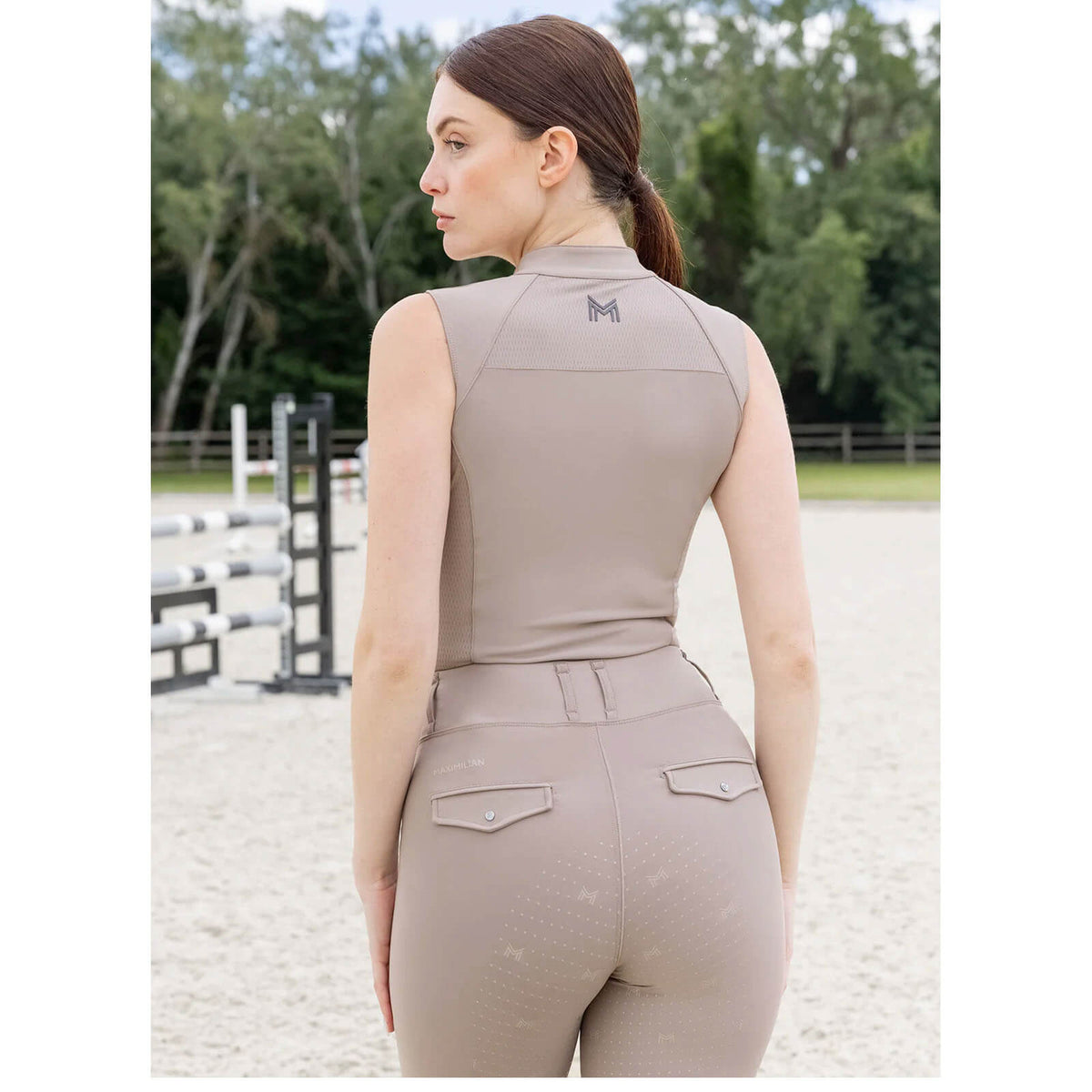 Maximilian Equestrian Funktionstop Miral Sleeveless Base Layer, Beige, Reiterin von hinten auf dem Reitplatz.