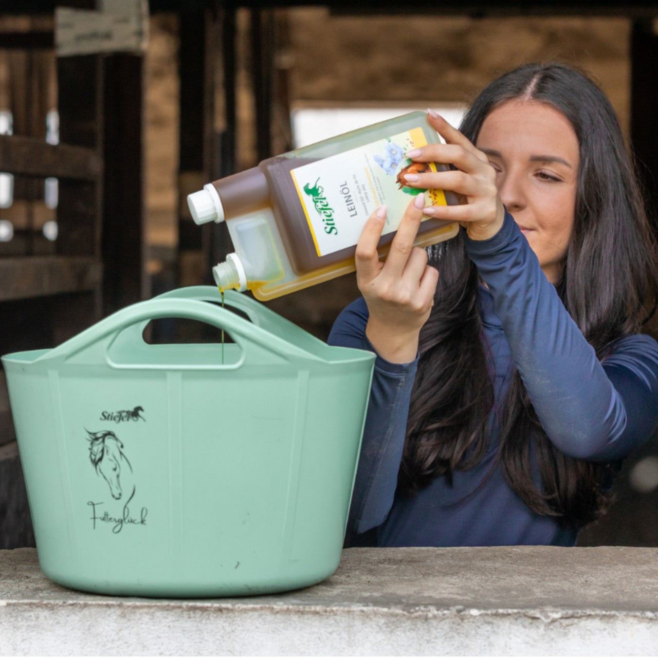 Stiefel Leinöl Einzelfuttermittel für Pferde, 1000 ml, Person gießt Produkt in einen Eimer.